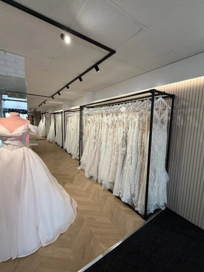 A displayed wedding gown beside rails of dresses in the boutique
