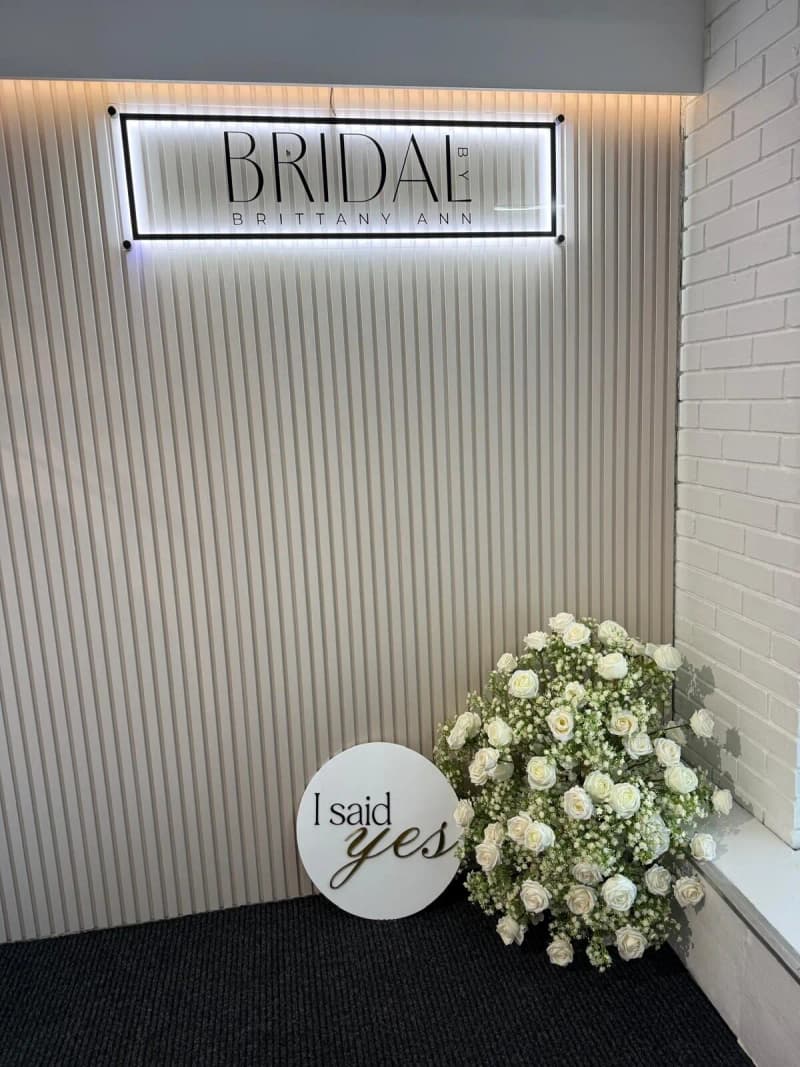 The illuminated Bridal by Brittany Ann sign beside white roses and an ‘I said yes’ sign