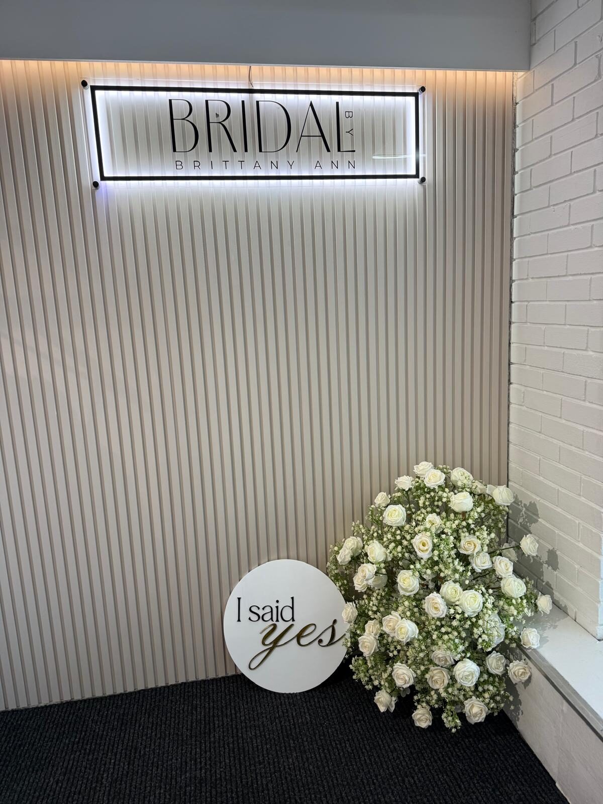The illuminated Bridal by Brittany Ann sign beside white roses and an ‘I said yes’ sign